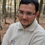 A man in glasses is standing in the woods.