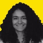 A woman with curly hair smiling in front of a yellow background.