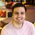 A smiling man in a pink shirt sitting in a lobby.