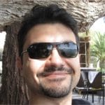 A man in sunglasses is smiling in front of a tree.