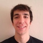 A young man smiling in front of a white wall.