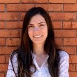 A woman smiling in front of a brick wall.